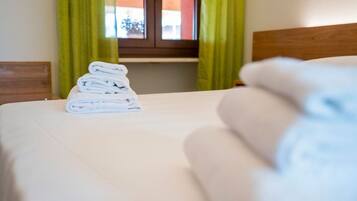 A neatly made bed with a stack of folded towels on the side.