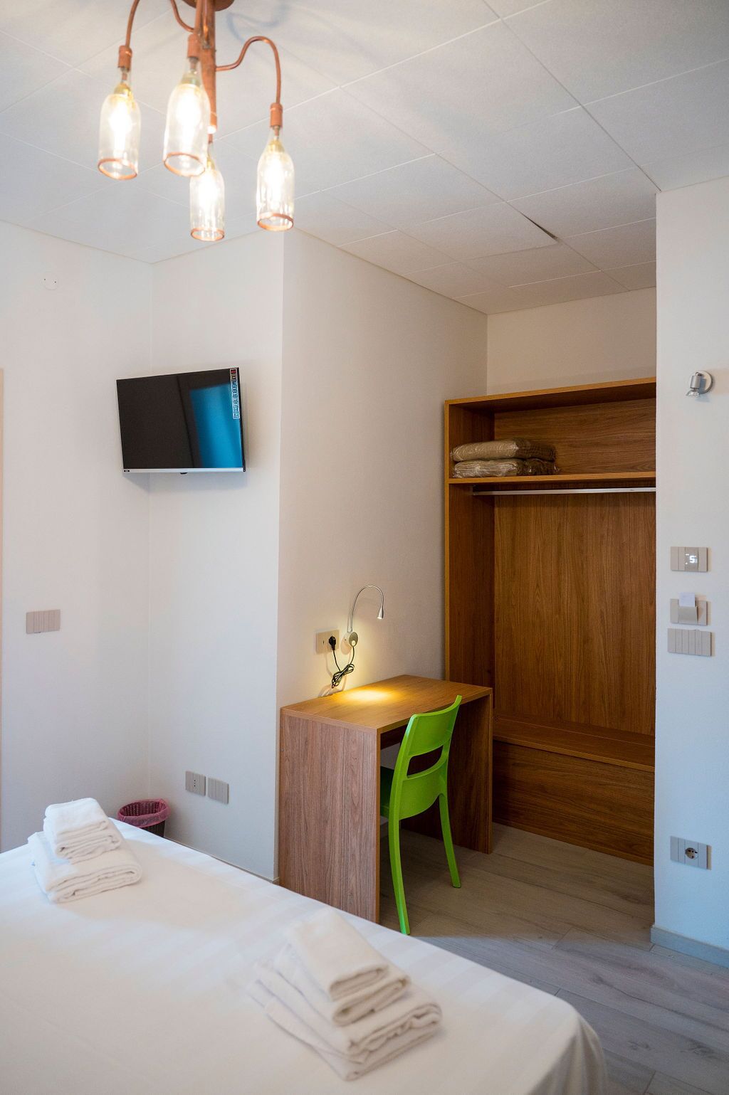 A hotel room with a bed, a desk with a chair, a television, and a wardrobe.