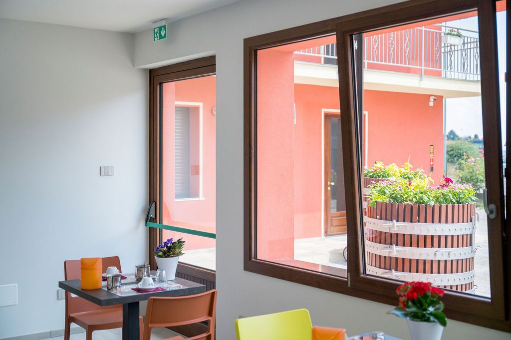 A room with a dining table, chairs, a potted plant, and a window with a view of an outdoor balcony and a planter.