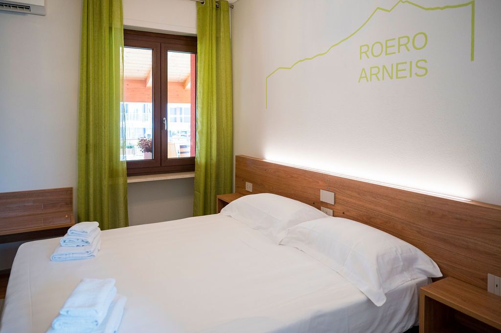 A hotel room with a bed, green curtains, a window, and a wall with a map.