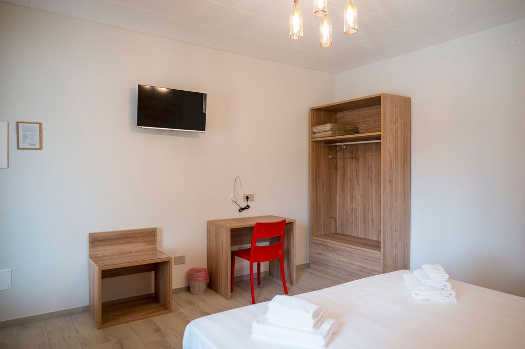 Una habitación de hotel con cama, escritorio, una silla roja, televisor y armario.