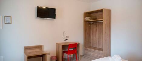 A hotel room with a bed, a desk, a red chair, a TV, and a wardrobe.