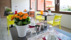 A dining area with a table set for two, featuring a white vase with orange flowers, clear glassware, and a menu. - Vino e Turismo (Cervasca)