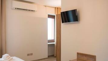 Una habitación de hotel con dos camas, un televisor montado en la pared, una silla de madera y una lámpara en el techo.