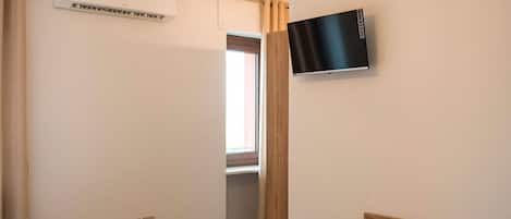Una habitación de hotel con dos camas, un televisor montado en la pared, una silla de madera y una lámpara en el techo.