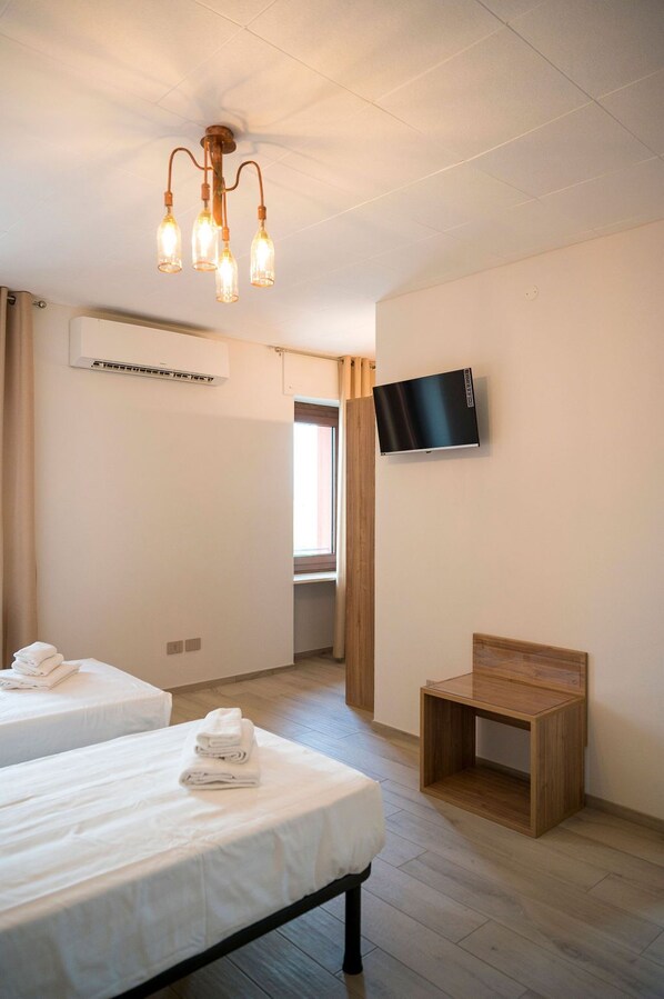 Una habitación de hotel con dos camas, un televisor montado en la pared, una silla de madera y una lámpara en el techo.