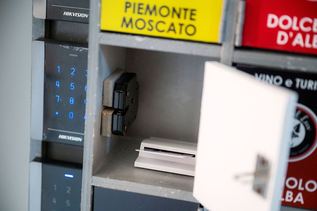 A vending machine with a numeric keypad and a coin slot, surrounded by various signs including "PIEMONTE MOSCATO" and "DOLCE D'ALBA".