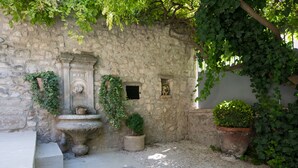 Eine Steinsäule mit Brunnen, Kübelpflanzen und einem Kieshof.