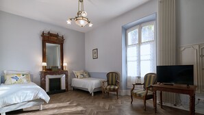 Ein Schlafzimmer mit einem Bett, zwei Stühlen, einem Fernseher, einem Kamin und einem großen Fenster.