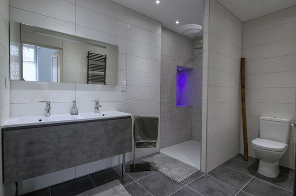Une salle de bain moderne dotée d’un meuble-lavabo à deux vasques, d’une douche à parois de verre et de toilettes.