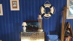 A room with a blue wall, a framed welcome sign, a lamp, a framed picture, a chair, and a bookshelf.