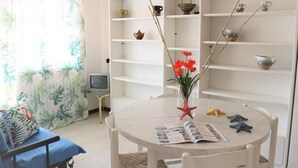 Ett rum med ett runt bord, en stol, en säng, en tv och hyllor med diverse föremål.