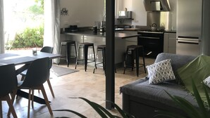 Een moderne keuken met een centraal eiland, een eethoek met tafel en stoelen, en een zithoek met bank en een plant.