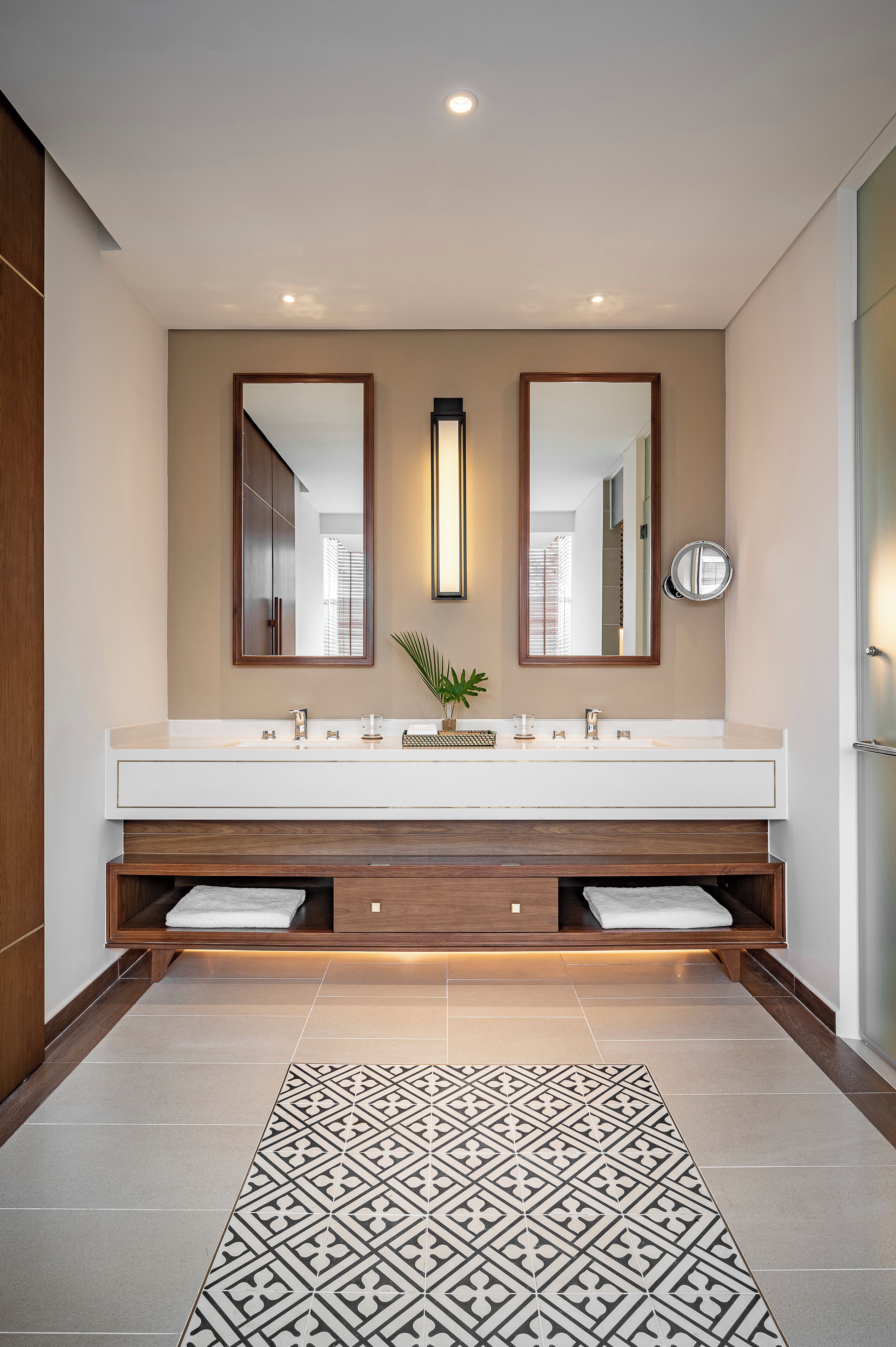A modern bathroom with a large mirror, two sinks, and a patterned rug.