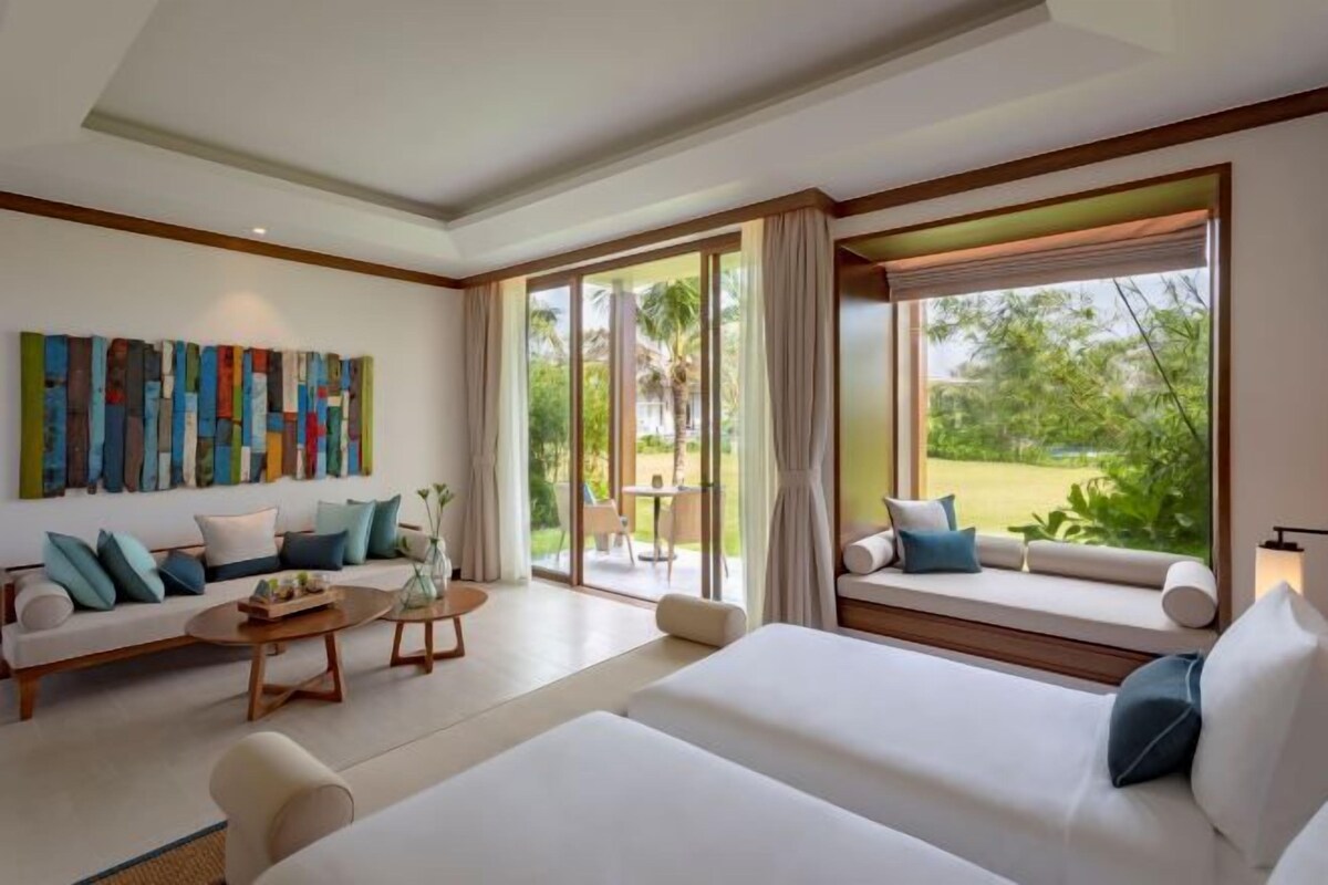 A modern hotel room with a large window, a sofa, a bed, and a coffee table.