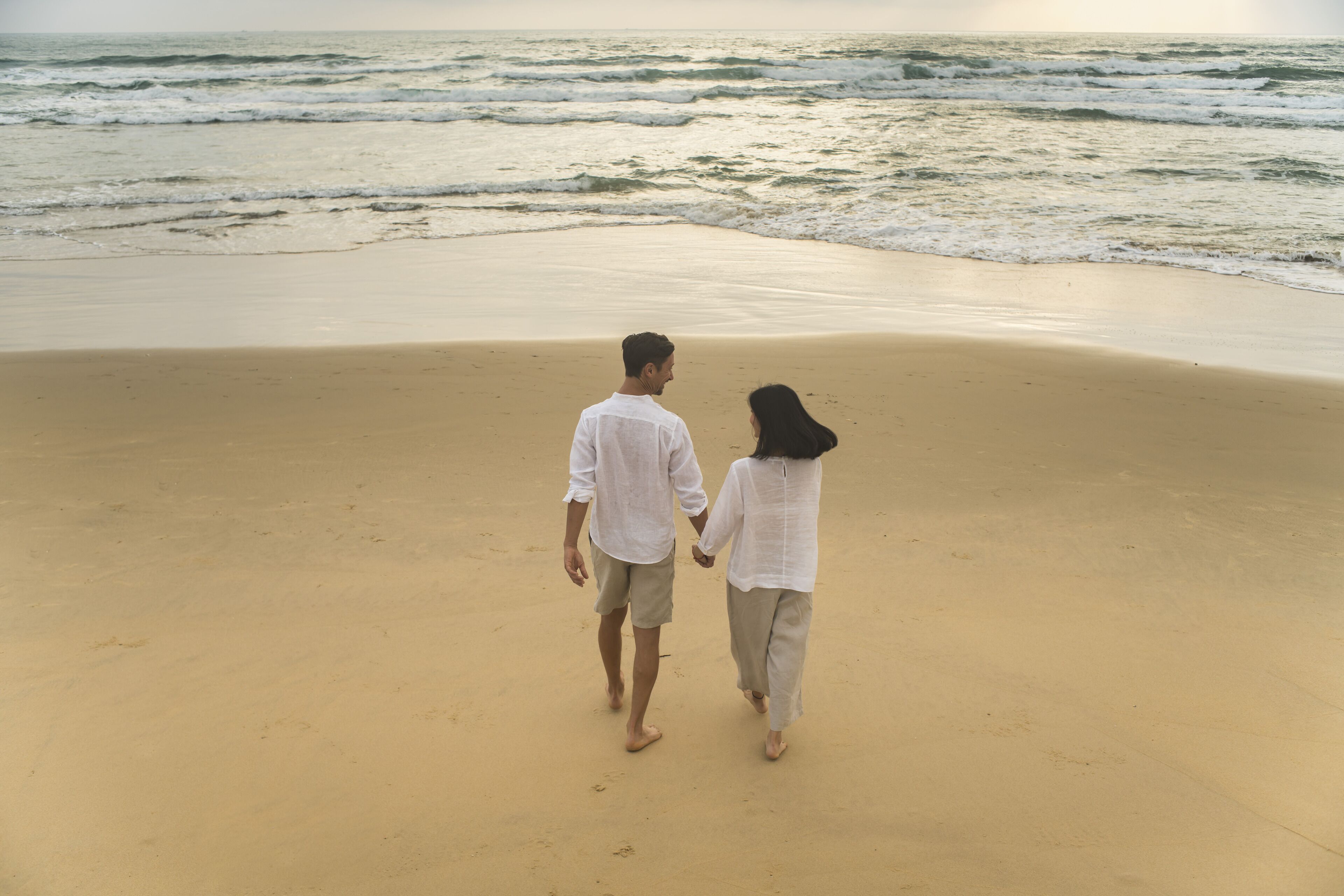 A couple walking on a sandy beach with the ocean in the background.