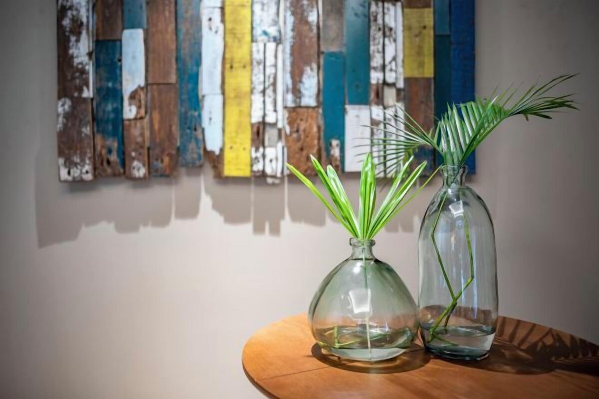 Two glass vases with green plants on a wooden table against a wall with colorful wooden planks.