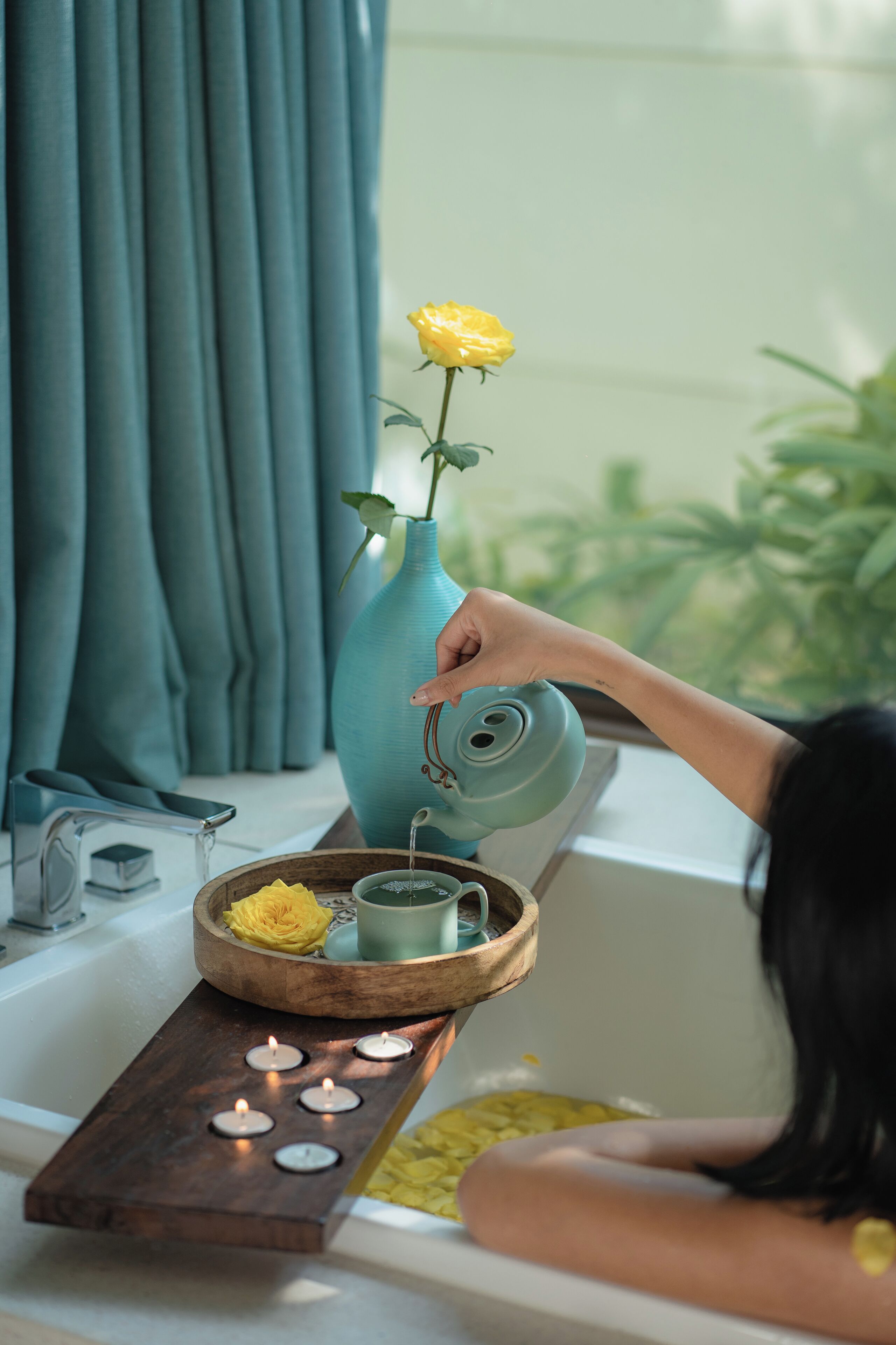 Una bañera con una bandeja de madera que sostiene velas, un florero con una flor amarilla y un calentador de agua.