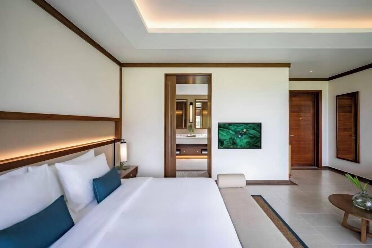 A modern hotel room with a large bed, a nightstand, a mirror, and a view into the bathroom.