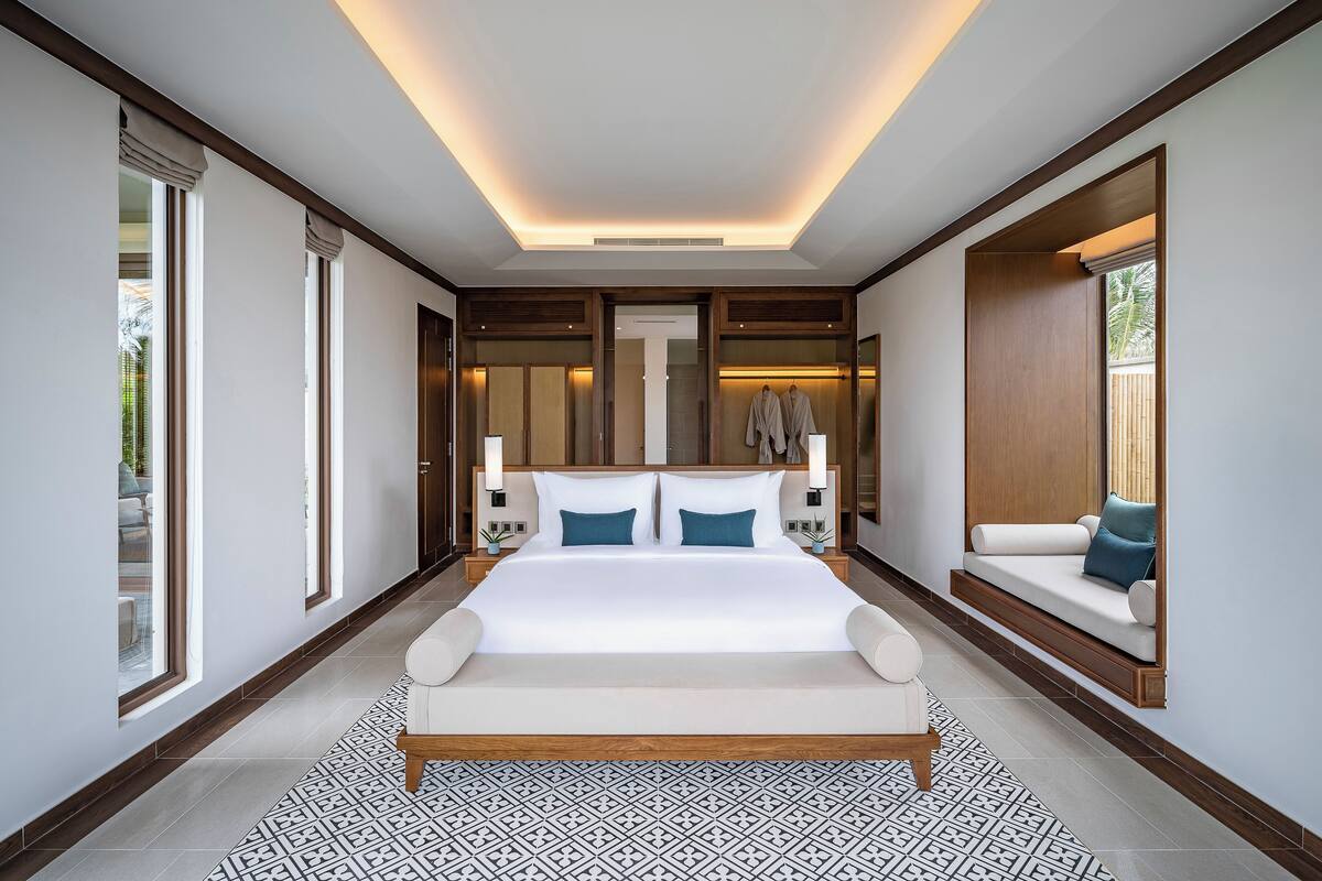 A modern bedroom with a large bed, a built-in bench, and a view of the outdoors.