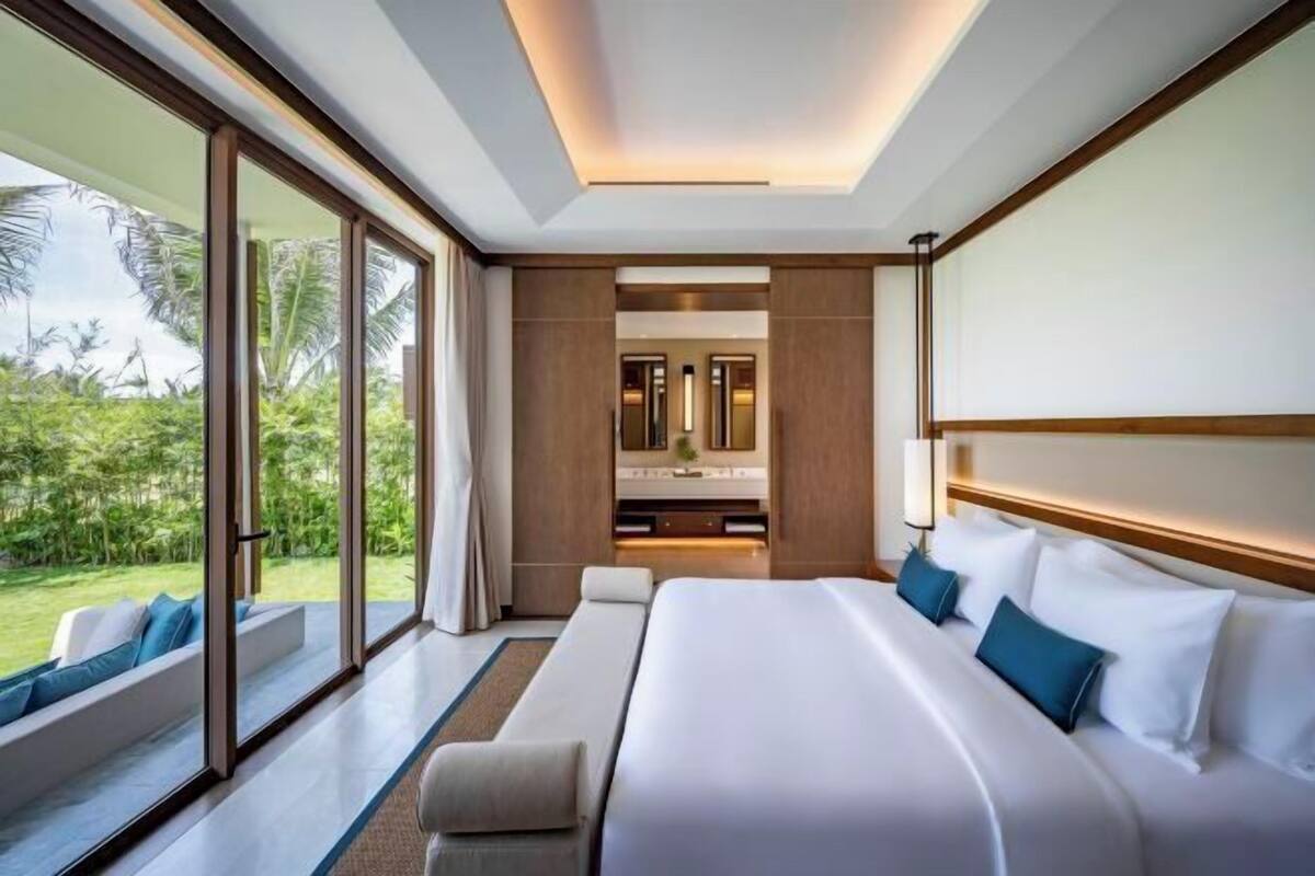 A modern hotel room with a large bed, a sitting area, and a view of the outdoors.