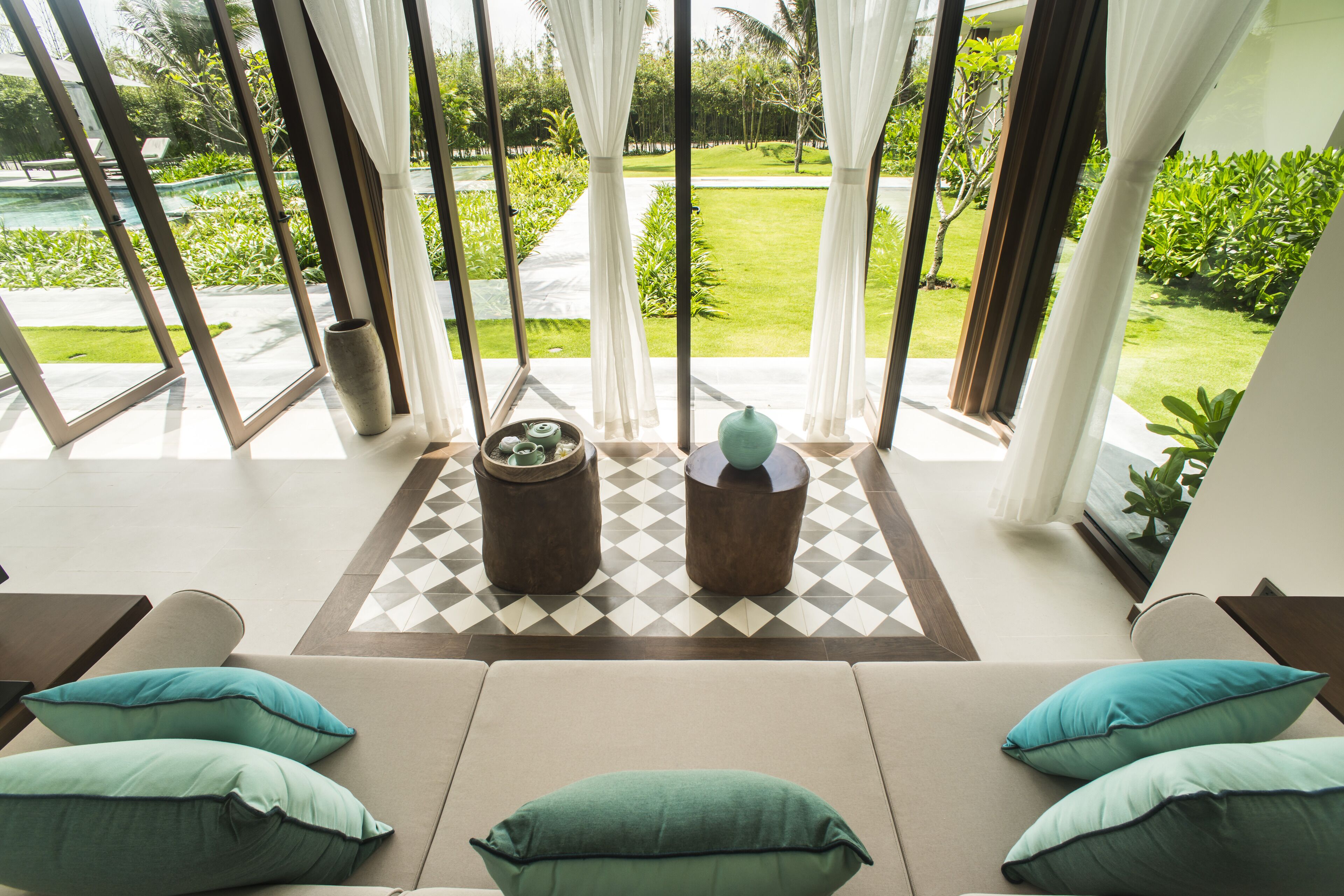 A modern room with a large window, a sofa with cushions, and two wooden side tables with decorative items.