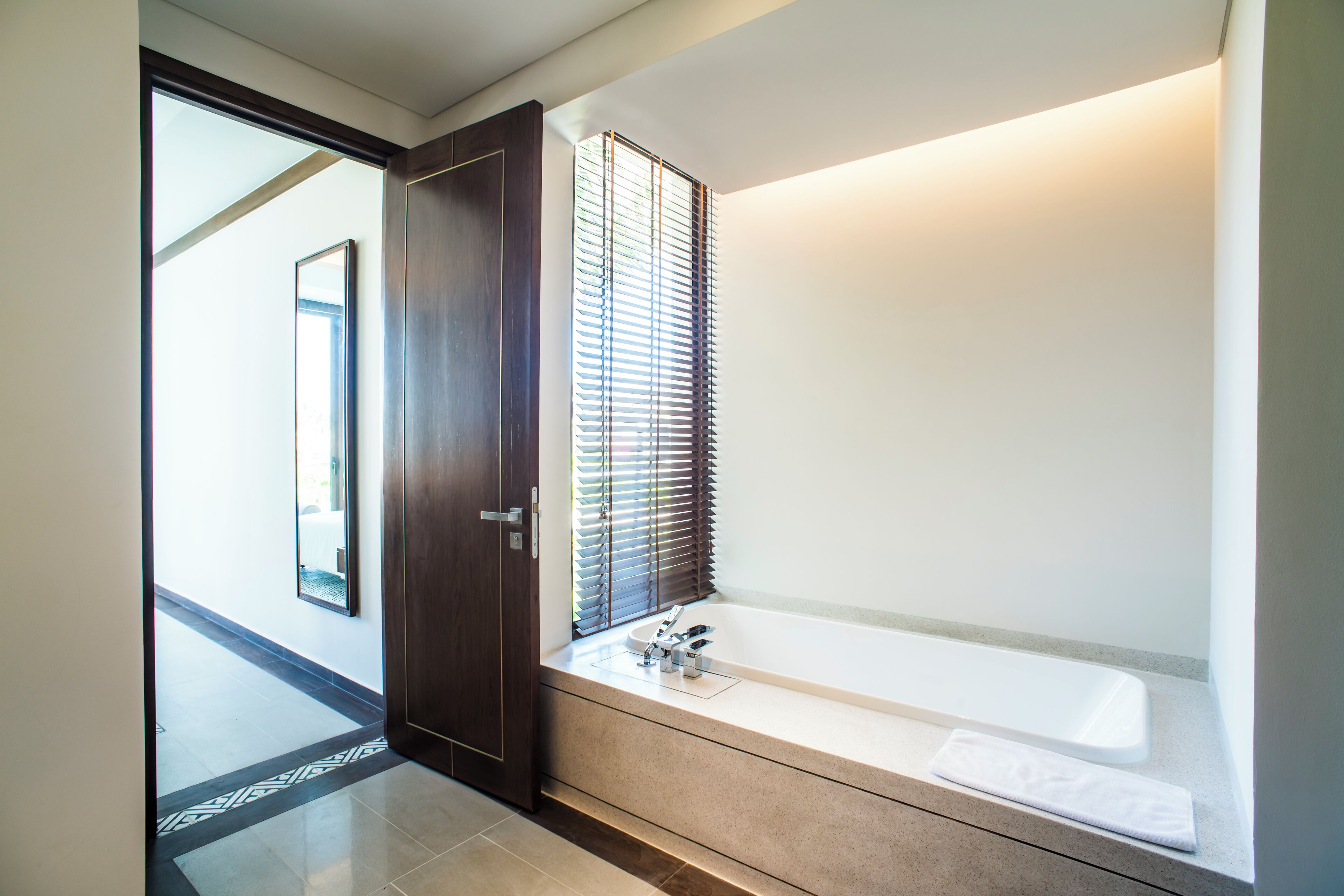 A modern bathroom with a large bathtub, a walk-in shower, and a window with blinds.