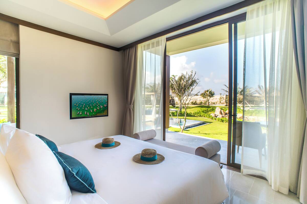 A hotel room with a large bed, a TV on the wall, and a view of a garden and pool.