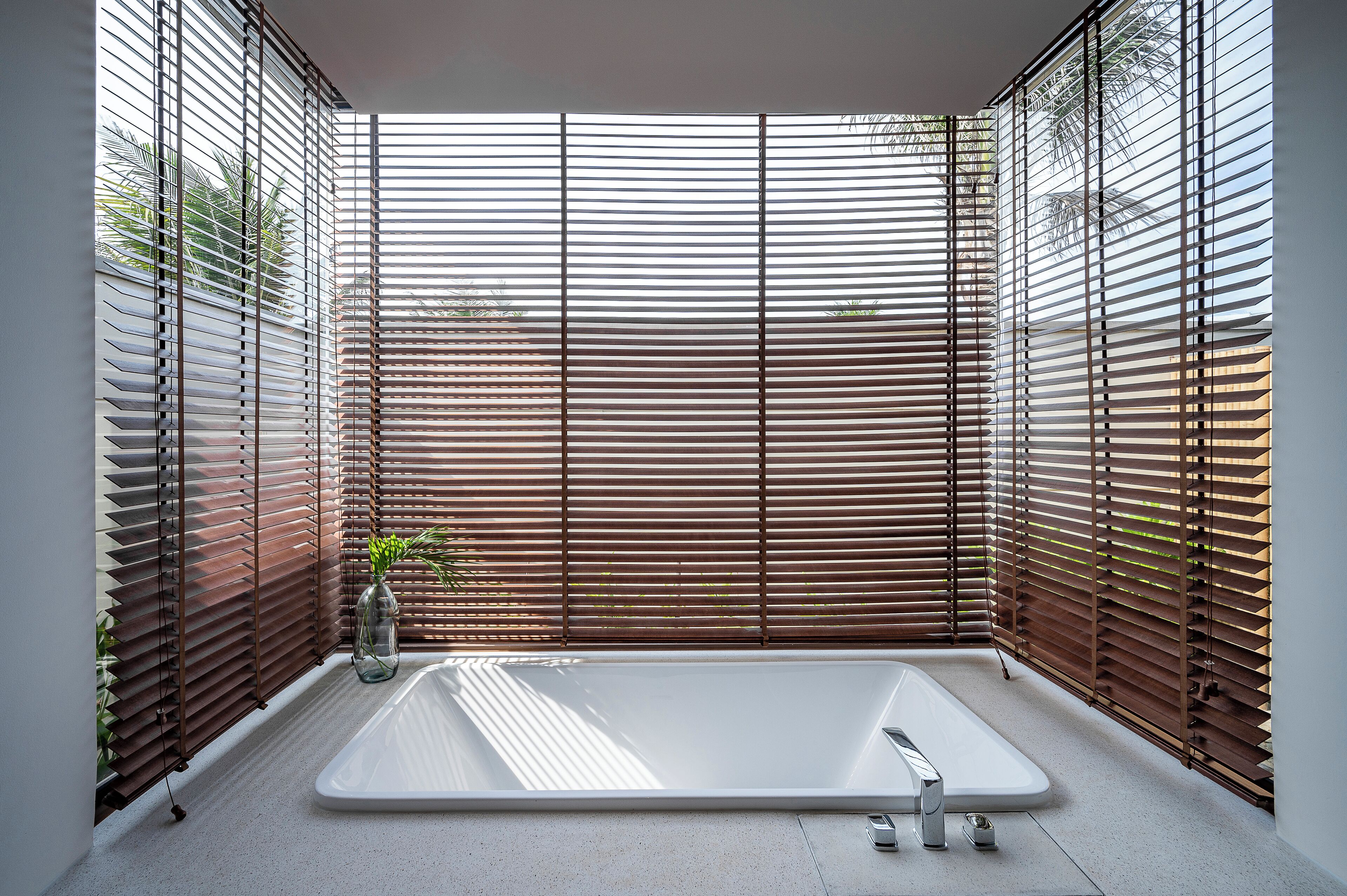 A modern bathroom with a freestanding bathtub, wooden blinds, and a potted plant.