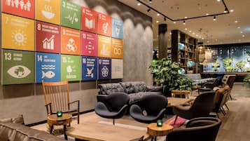 A modern lounge area with comfortable seating, a wall displaying the UN Sustainable Development Goals, and a well-lit interior with plants.