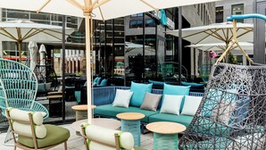 An outdoor seating area with a sofa, chairs, and tables under umbrellas. - Motel One Bonn-Hauptbahnhof (Bonn)