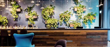A modern bar area with wooden paneling, hanging plants, and contemporary chairs.