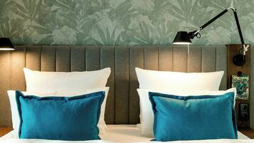 A hotel room with a bed, two pillows, a nightstand, a lamp, and a wall with a floral pattern.