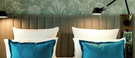 Habitación de hotel con una cama, dos almohadas, una mesita de noche, una lámpara y una pared con estampado floral.