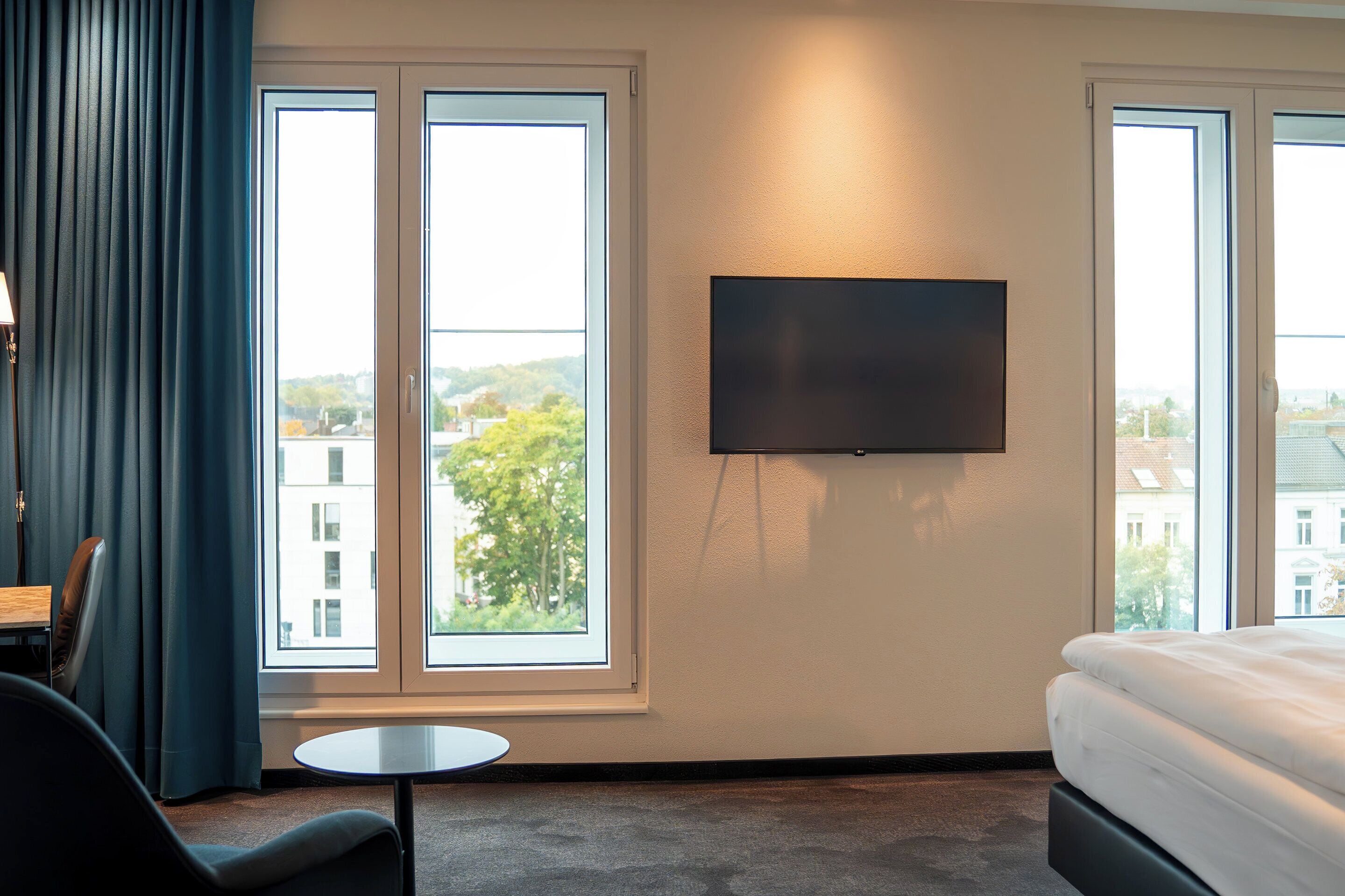 A hotel room with a bed, a TV mounted on the wall, a small table, and a chair.