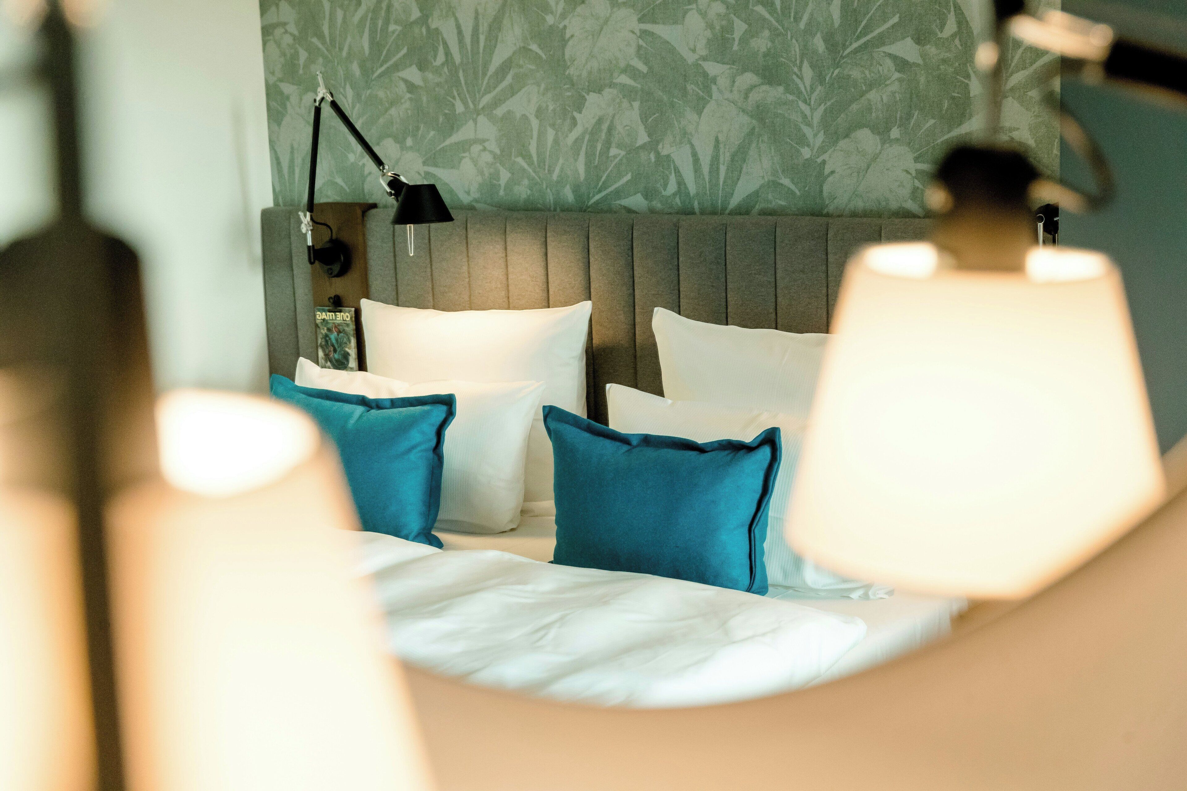 Una habitación de hotel con una cama, almohadas, una lámpara y una pared con estampado floral.