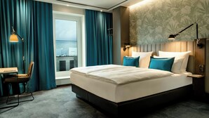 A modern hotel room with a large bed, a desk, and a view of the city. - Motel One Bonn-Hauptbahnhof (Bonn)