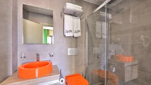 A modern bathroom with a large orange sink, a glass shower enclosure, and a mirror above the sink. - Zeytin Hotel (Kas)