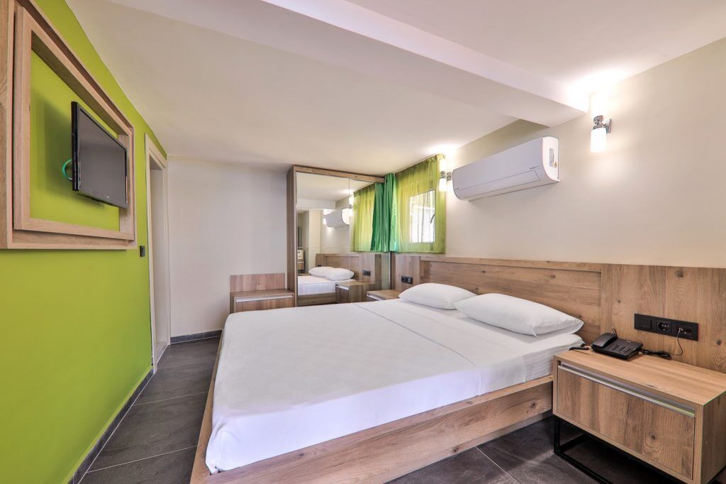 Habitación de hotel con una cama grande, mesitas de noche, un televisor de pantalla plana, un equipo de aire acondicionado y un espejo.
