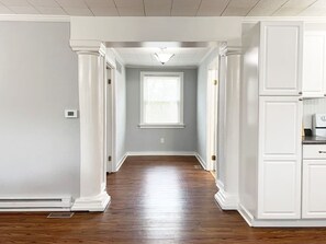 A hallway with white walls, a wooden floor, and a window with blinds. - Fox Haus near Purina, WashMo, I-44, Dog Friendly (Villa Ridge)