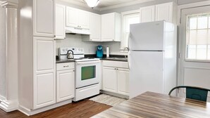 Une cuisine avec des meubles blancs, une cuisinière, un réfrigérateur et une table à manger.