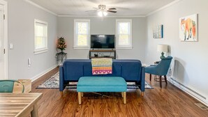 Un salon avec un canapé bleu, un plancher en bois, un ventilateur de plafond, un téléviseur et un sapin de Noël.