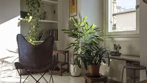 A room with a leather chair, a large potted plant, a small table, and a window with a view of buildings. - Charming apartment 2 bdrs in Brera district (Milano)