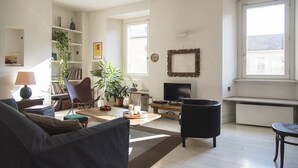 A living room with a sofa, armchair, TV, bookshelf, and a large window. - Charming apartment 2 bdrs in Brera district (Milano)