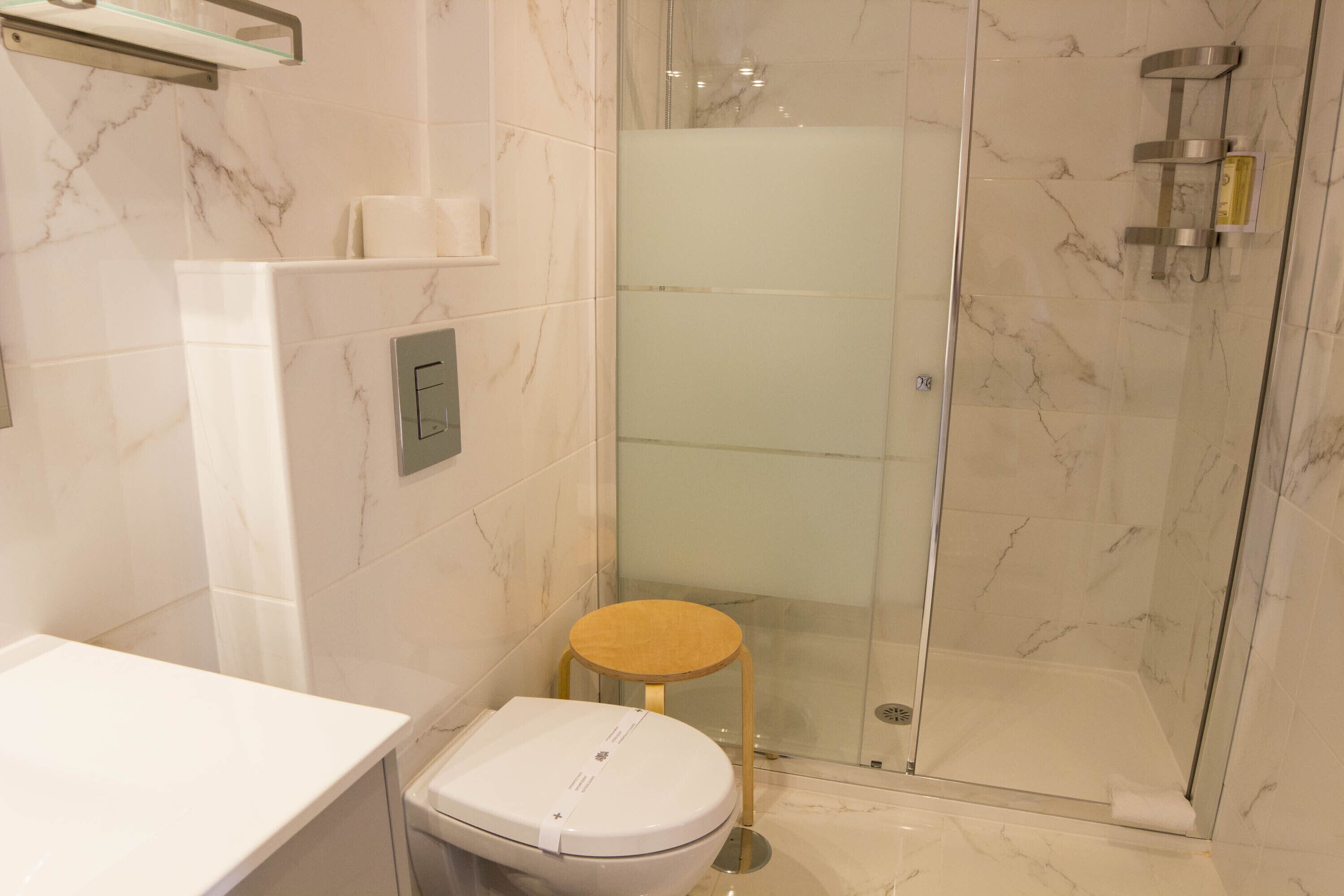 Ein modernes Badezimmer mit einer gläsernen Duschkabine, einer Toilette und einem kleinen hölzernen Hocker.
