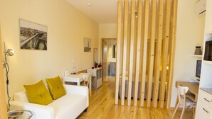 A modern hotel room with a white sofa, a small round table, a wooden partition, and a desk with a chair. - Cedofeita Back Garden (Porto)