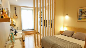 A bedroom with a bed, a wooden headboard, a nightstand, a lamp, a wall-mounted guitar, and a window with a view of the outside. - Cedofeita Back Garden (Porto)