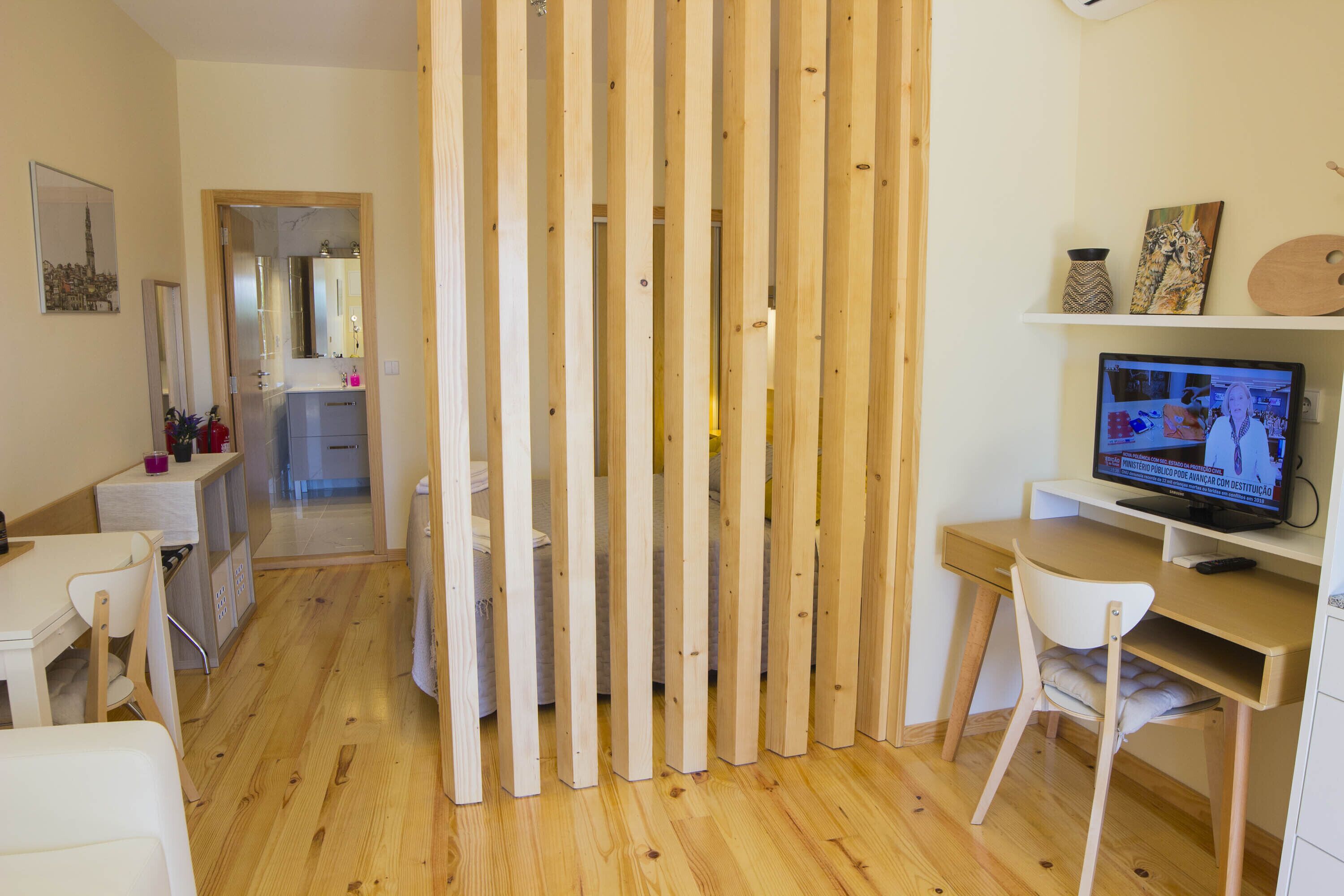 A room with a wooden partition, a desk with a computer, a chair, and a small shelf with decorative items.
