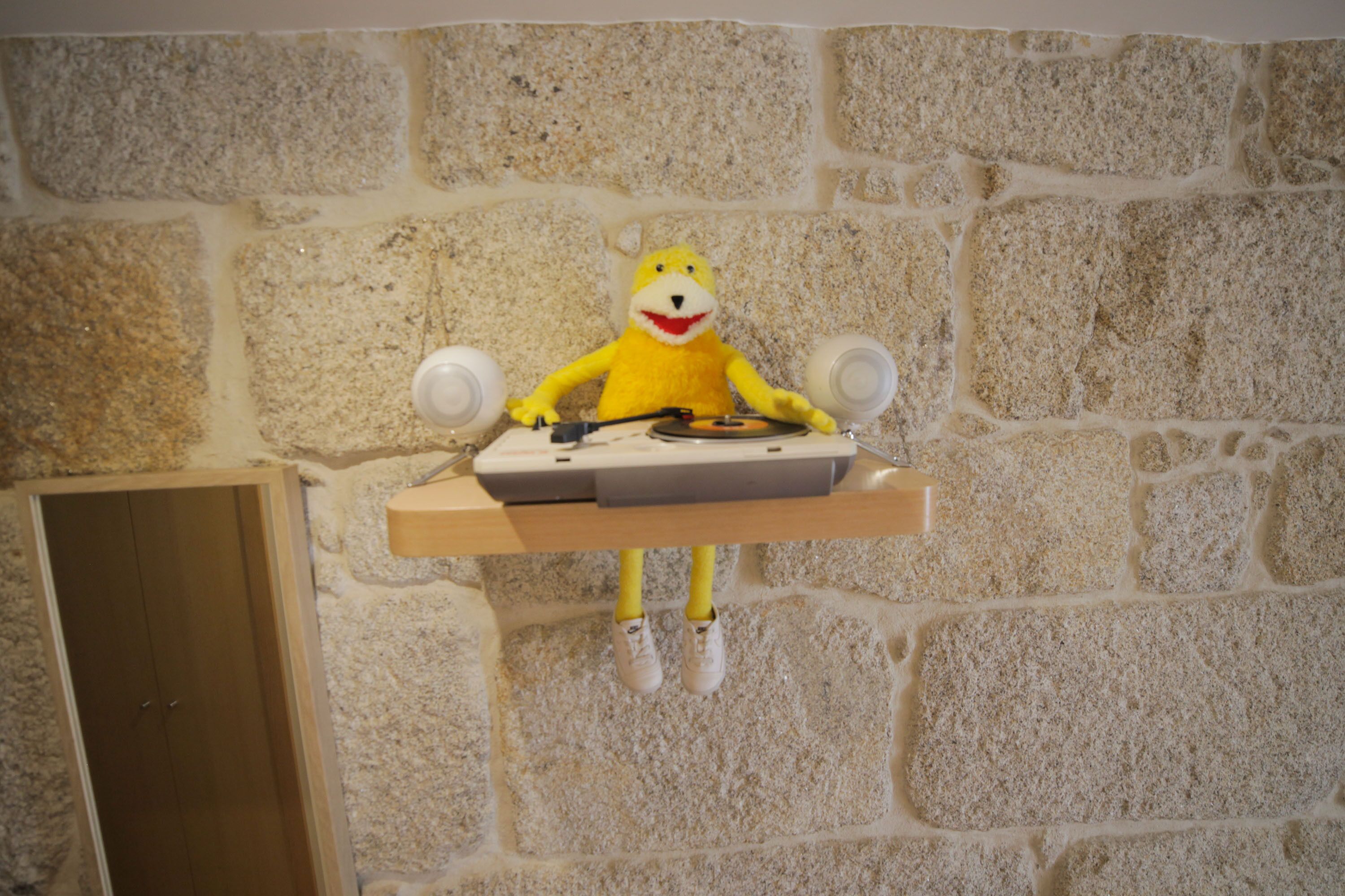 Un peluche sobre una estantería frente a una pared de piedra.
