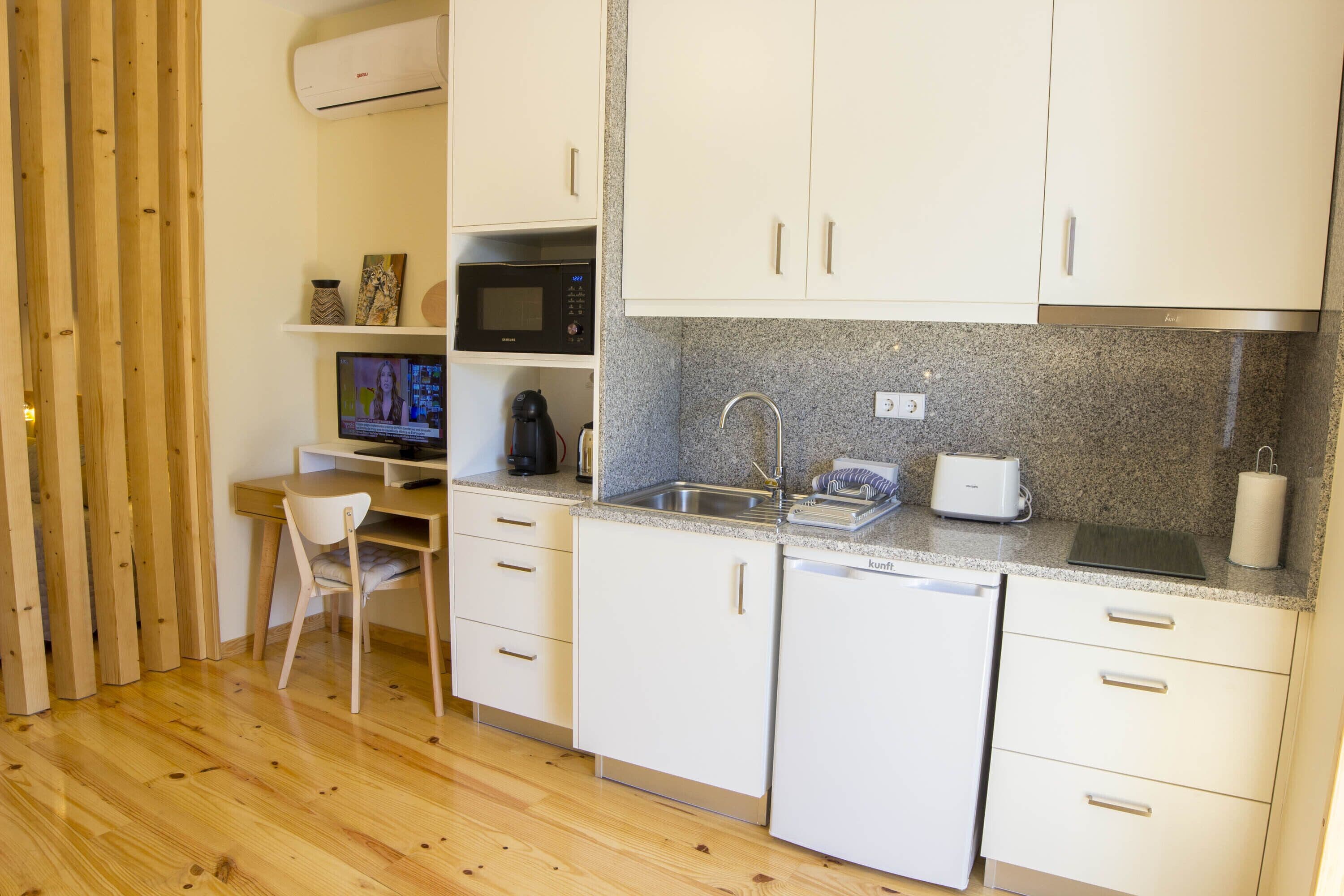 A compact kitchen with white cabinets, a granite countertop, a microwave, a toaster, and a sink.
